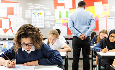 Sch�lerinnen schreiben einen Test. Ein Lehrer, mit dem R�cken zur Kamera, beaufsichtigt sie. Bild: rawpixel.com | Adobe Stock