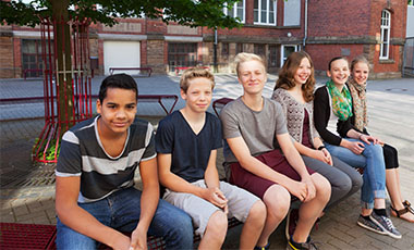 Eine Gruppe von Sch�lerinnen und Sch�lern sitzt unter einem Baum auf einem Schulhof. Bild: Christian Schwier | Adobe Stock