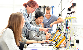 Eine kleine Gruppe von Jugendlichen vor einem Pult mit elektronischen Anlagen, stehend daneben eine Ausbilderin