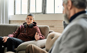 Ein Junge sitzt auf einem Sofa. Mit im Bild sein Gesprchspartner, ein Berater. Bild: Svitlana | Adobe Stock