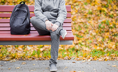 Auf einer Parkbank im Herbst sitzt allein ein Junge. Sein Gesicht ist nicht zu sehen.