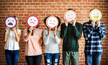 F�nf junge Menschen halten sich Bilder von Emojis vors Gesicht, die verschiedene Gef�hlszust�nde ausdr�cken.
