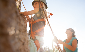 Mdchen klettert an einem Felsen, im Hintergrund eine weibliche Erwachsene, die das Sicherungsseil hlt