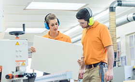 Auszubildende und Ausbilder, sie h�lt mit beiden H�nden eine Paneele, beide tragen Kopfh�rer als L�rmschutz