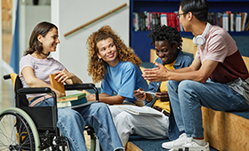 M�nnliche und weibliche Jugendliche, zum Teil mit dunkler Hautfarbe oder im Rollstuhl, sitzen zusammen in einem Raum und reden