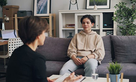 Eine junge Person sitzt auf einem Sofa und wird von einer �lteren Person beraten