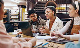Eine Gruppe von jungen Menschen verschiedener Hautfarben rund um einen Tisch