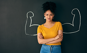Jugendliche vor einer Tafel, darauf hinter ihr mit Kreide aufgemalt muskelbepackte Arme mit den Unterarmen nach oben gerichtet