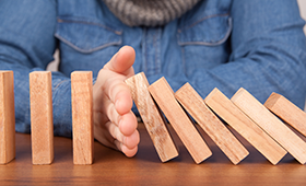 Eine Hand stoppt eine Reihe von fallenden Dominosteinen