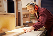 Jugendliche schneidet an einer Werkbank ein Holzbrett zu Jugendliche schneidet an einer Werkbank ein Holzbrett zu