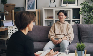 Eine junge Person sitzt auf einem Sofa und wird von einer �lteren Person beraten.
