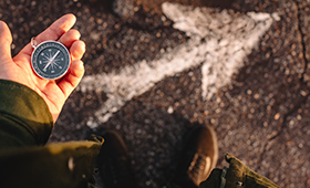 Eine Hand h�lt einen Kompass, auf dem Asphalt darunter ist ein wei�er Pfeil zu sehen