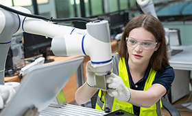 Auszubildende in Schutzkleidung legt ihre H�nde an den Schwenkarm eines Roboters