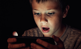 Junge starrt mit weit aufgerissenen Augen auf den Monitor seine Smartphones
