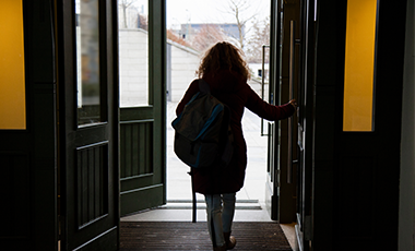 Eine Person verlässt ein Gebäude durch die Tür. Gebäude und Person liegen im Schatten. Eine Person verlässt ein Gebäude durch die Tür. Gebäude und Person liegen im Schatten.