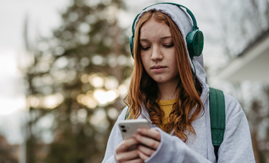 Jugendliche blickt skeptisch auf ihr Smartphone, das sie in beiden Händen hält Jugendliche blickt skeptisch auf ihr Smartphone, das sie in beiden Händen hält