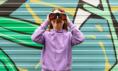 Eine junge Frau h�lt ein Fernglas vor ihre Augen und l�chelt.