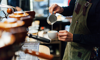 Barista bereitet in einem Café eine Tasse Cappuccino zu, indem er Milchschaum darüber gießt Barista bereitet in einem Café eine Tasse Cappuccino zu, indem er Milchschaum darüber gießt