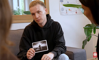 Junger Mann h�lt im Beisein anderer junger Leute ein Foto vor seine Brust, damit diese es sich ansehen k�nnen