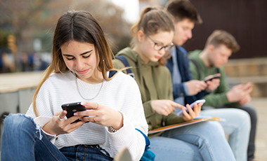Vier M�dchen und Jungen sitzen auf einer Mauer und schauen auf ihre Smartphones