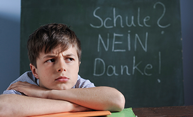 Junge mit skeptisch verzogenem Gesicht vor einer Schultafel, auf der steht: "Schule, nein danke!" Junge mit skeptisch verzogenem Gesicht vor einer Schultafel, auf der steht: "Schule, nein danke!"