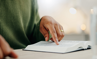 Person hat ein Buch vor sich auf einem Tisch und legt einen Zeigefinger auf die Zeilen Person hat ein Buch vor sich auf einem Tisch und legt einen Zeigefinger auf die Zeilen