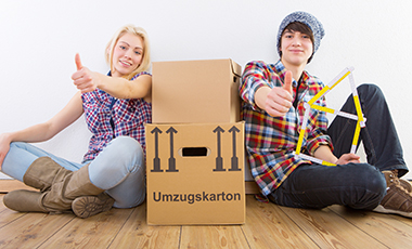 Zwei Jugendliche (männlich und weiblich) sitzen neben einem Umzugskarton und recken ihre Daumen nach oben Zwei Jugendliche (männlich und weiblich) sitzen neben einem Umzugskarton und recken ihre Daumen nach oben
